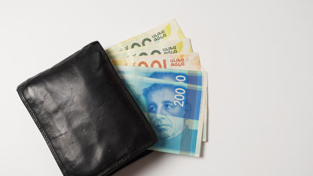 Black wallet with colorful Shekel banknotes inside on white backgroundの写真素材