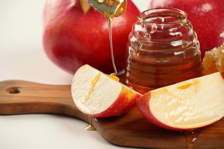 Jewish holiday Rosh Hashana celebration. Pomegranate, apples and honey traditional products for the holyday. Pouring honey on apple and pomegranateの写真素材