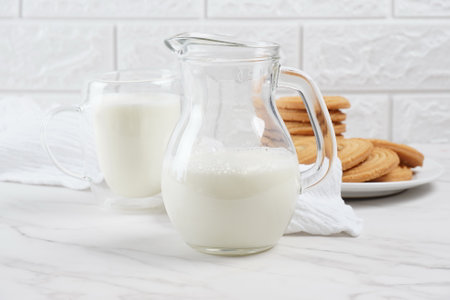 Milk in a transparent glass and jar on a marble table. Round ring shaped German spritz biscuits at backgroundの写真素材