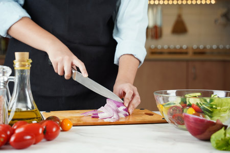 The woman in the process of making vegetable salad. Closeup of hands  cutting red onions on wooden tableの写真素材