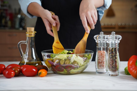 Girl mixing salad with wooden spoons. The Girl in the process of making vegetable salad.の写真素材