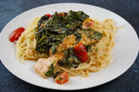 Salmon Fillet in creamy sauce with spaghetti, cream cheese and spinach and cherry tomatoes close-up on plateの写真素材