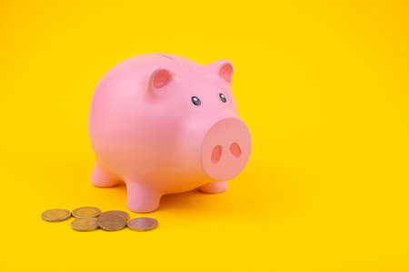 pink piggy bank on a yellow background with lying coins.の写真素材