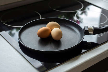 three raw eggs are lying in a frying pan in the kitchen.の写真素材