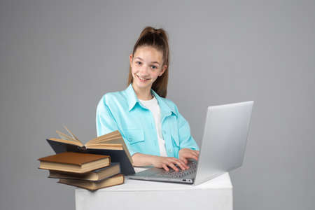A beautiful smiling teenage girl sitting and studying with a laptop and books.の写真素材