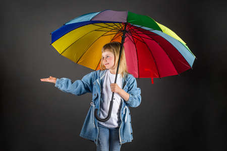 The girl smiles, holds a multicolored rainbow umbrella in her hands and checks if it is raining.の写真素材