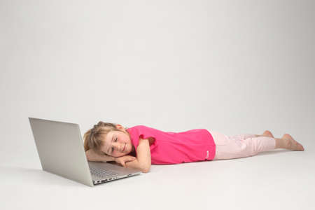 A little girl with her eyes closed lies at the computer and smiles.