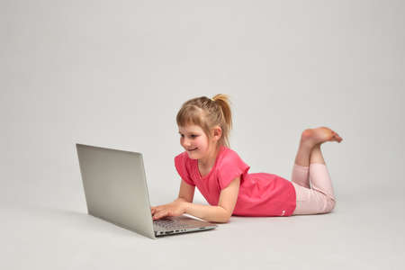 A little smiling girl lies and looks at the computer.