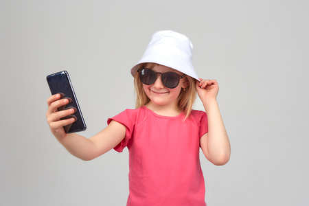 Funny girl in sunglasses and white hat smiles and takes a selfie.の写真素材