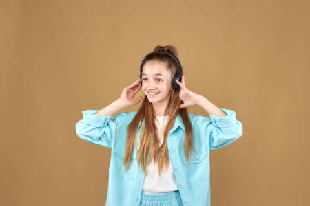 A young beautiful smiling teenage girl listens to music in black headphones and holds her hands to the headphones.の写真素材