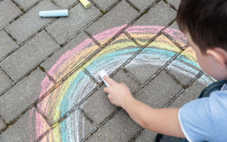 Portrait of a child drawing a rainbow on the street with colored chalk. selective focus. kid. A child is playing outside.の写真素材