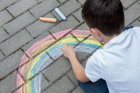 Portrait of a child drawing a rainbow on the street with colored chalk. selective focus. kid. A child is playing outside.の写真素材