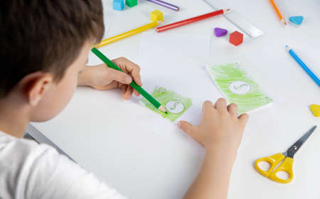 A little boy enthusiastically draws toy money with colored pencils for the game. family budget....