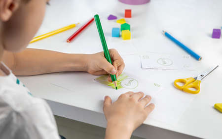 A little boy enthusiastically draws toy money with colored pencils for the game. family budget. economy. money. The kid draws. economic crisis. Kids play.の写真素材