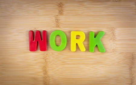The word work is laid out of multicolored letters on a table background with a wood texture. concept. game. workの写真素材