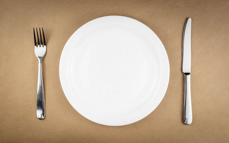 Empty plate with fork and knife isolated on brown recycled paper background with copy space.の写真素材