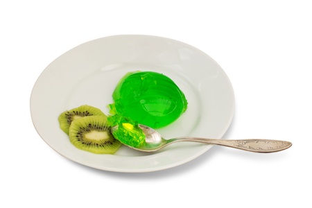 Green jelly with kiwi slices and a silver spoon on a white plate isolated on white background