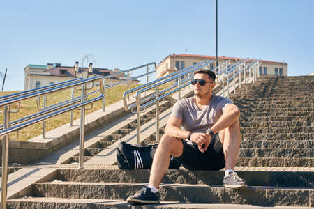 Athletic handsome man in shorts and sunglasses sits on the stairs after a sports workoutの写真素材