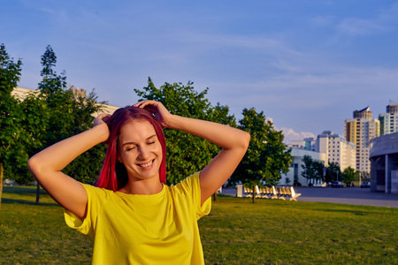 young woman with pink hair, yellow crop top closed her eyes, smiling in city parkの写真素材
