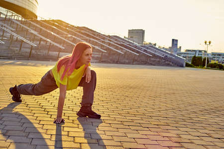 beautiful young woman with pink hair is sitting on the lawn in a city park and smilingの写真素材