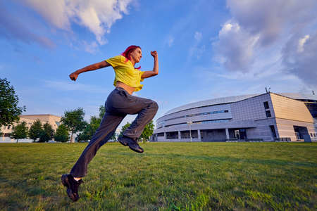 beautiful young woman with pink hair is sitting on the lawn in a city park and smilingの写真素材