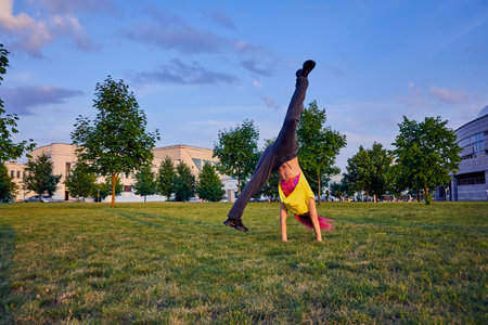 beautiful young girl with dyed pink hair, yellow crop top trains handspring in a city parkの写真素材