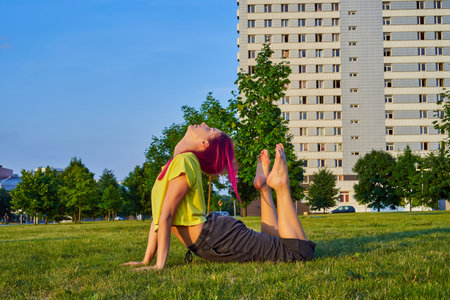 beautiful young girl with pink hair, yellow tank top trains stretching in park