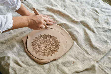 master craftsman rolls clay on the table, transfers napkin pattern to clay mass