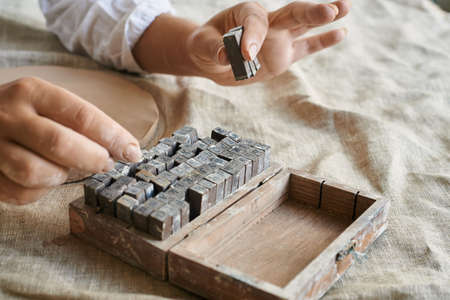 the woman's hands pick up letters to be printed on clay