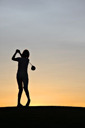 Female golfer swinging a driver at sunrise.の写真素材