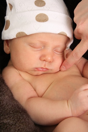 Newborn baby boy wearing a polka dot hat. Mom's finger is touching his cheek. の写真素材