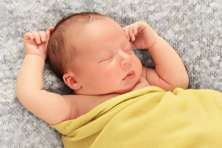 Newborn baby boy asleep wrapped in a yellow blanket.の写真素材
