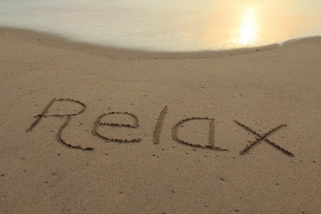 The word relax hand written in the sand at sunset  の写真素材