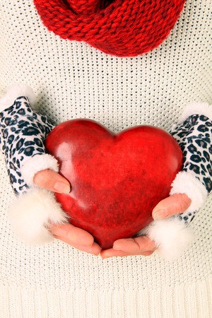 Close up of woman in winter sweater, scarf and gloves, holding a valentine heart  の写真素材