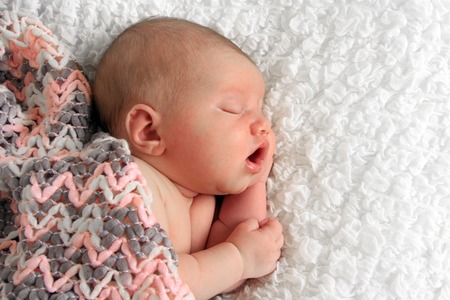 Newborn baby girl asleep on a white blanket.の写真素材