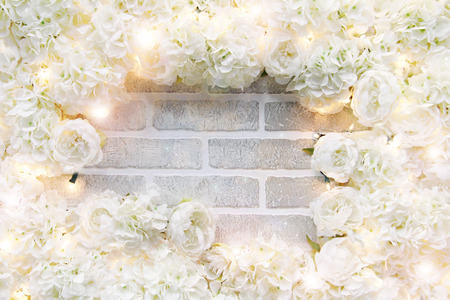 A frame of white roses and sparkling lights on a brick wall with copyspace in the center.の写真素材