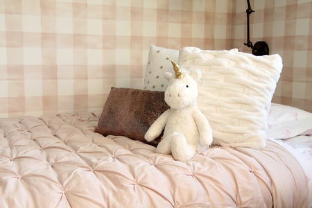 Unicorn stuffed toy leaning against bed cushions in a girls bedroom.の写真素材