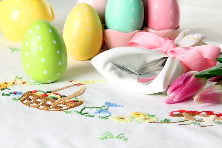 Easter place setting on an elegant linen table cloth.  This traditional holiday brunch place setting includes painted eggs, an embroidered Easter basket, silver cutlery wrapped in a napkin and springtime pink tulips. の写真素材
