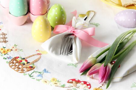Easter place setting on an elegant linen table cloth.  This traditional holiday brunch place setting includes painted eggs, an embroidered Easter basket, silver cutlery wrapped in a napkin and springtime pink tulips. の写真素材