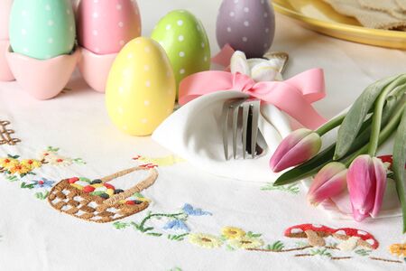 Easter place setting on an elegant linen table cloth.  This traditional holiday brunch place setting includes painted eggs, an embroidered Easter basket, silver cutlery wrapped in a napkin and springtime pink tulips.の写真素材