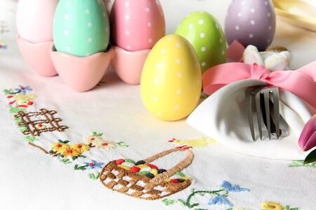 Easter place setting on an elegant linen table cloth.  This traditional holiday brunch place setting includes painted eggs, an embroidered Easter basket, silver cutlery wrapped in a napkin and springtime pink tulips. の写真素材