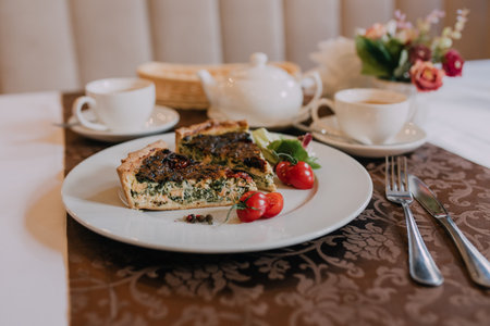 Slices of quiche with spinach and cherry tomatoes on a white plateの写真素材