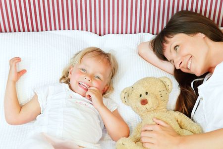 Mother and daughter lying in bed and smiling happily.の写真素材