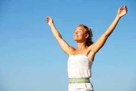 Beautiful young woman with arms raised on blue sky backgroundの写真素材
