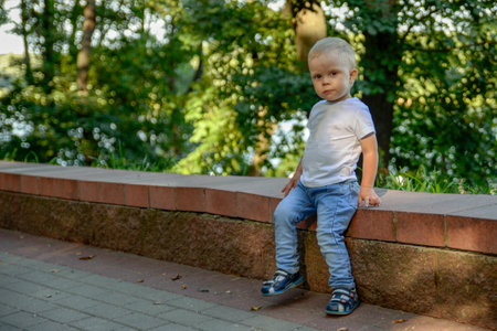 A boy in blue jeans sits on a parapet in a park in the summerの写真素材