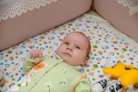 A small child lies in a cot with toysの写真素材