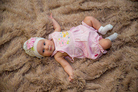 A girl in a pink dress and a cap with a flower rests on a brown plaid.の写真素材