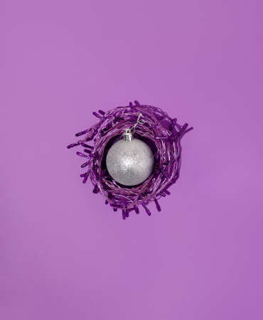 Creative concept with shiny silver bauble wrapped in Christmas light bulbs on a beautiful purple background. Minimal New Year composition.の写真素材