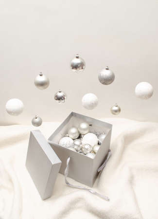 Silver an white Christmas tree baubles falling in grey present box on white background. Creative composition for New Year giving.の写真素材