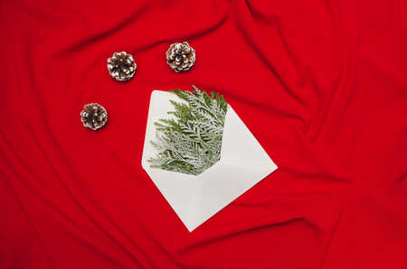 Christmas composition on red canvas with frozen cypresses and pinecones in an white envelope ready to send a New Yearâs greeting card. Minimal Christmas Idea.の写真素材